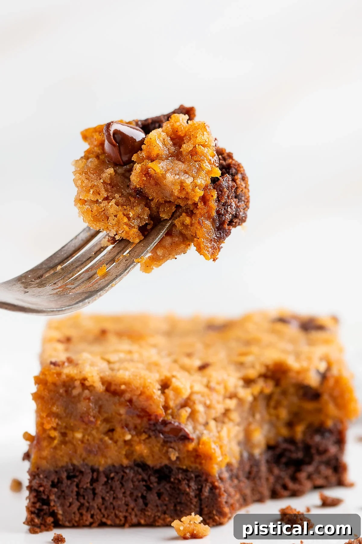 A fork lifts a delicious bite of Chocolate Pumpkin Cheesecake Bar, held above another bar on a white plate, highlighting the inviting layers.