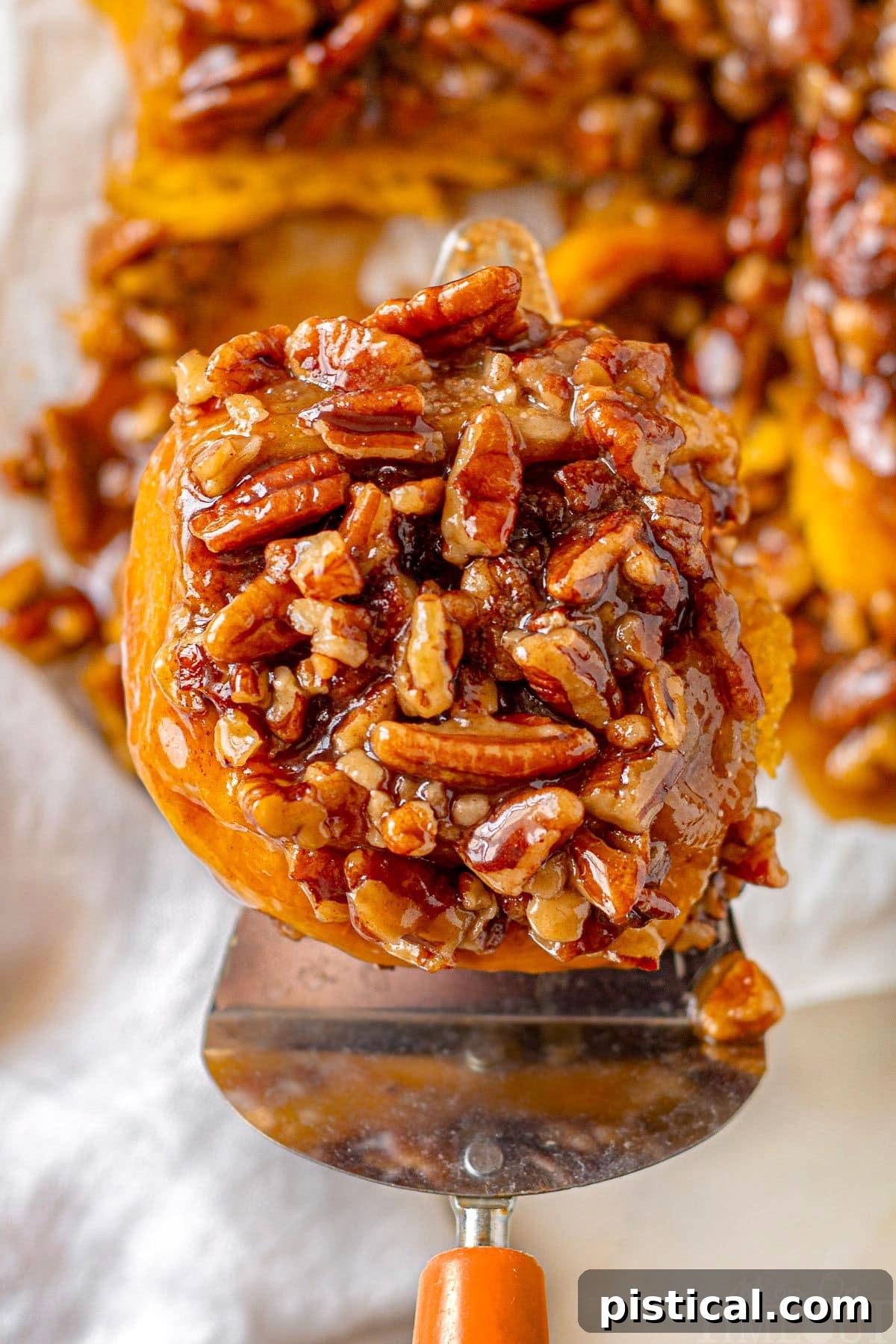 A freshly baked pumpkin sticky bun being carefully lifted from a cutting board, revealing its gooey caramel bottom and ready to be savored.