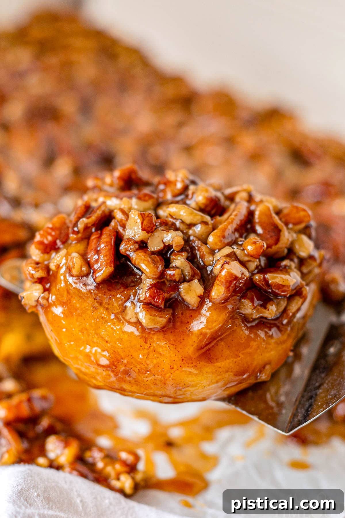 A perfectly baked pumpkin sticky bun is being carefully lifted from a serving board, its caramel glaze glistening, ready to be presented and enjoyed.