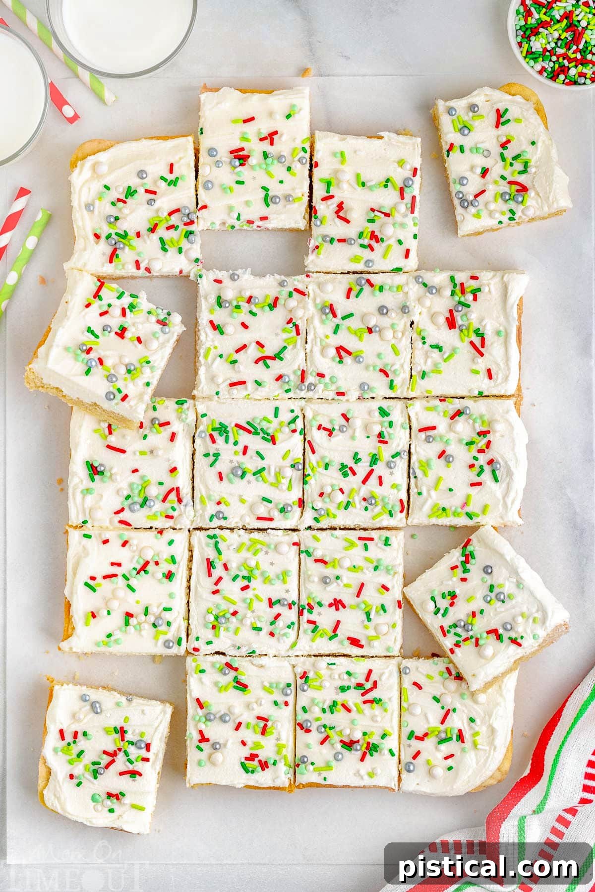 A top-down view of a batch of freshly baked and frosted Christmas Sugar Cookie Bars, cut into perfect squares and arranged on a sheet of parchment paper.