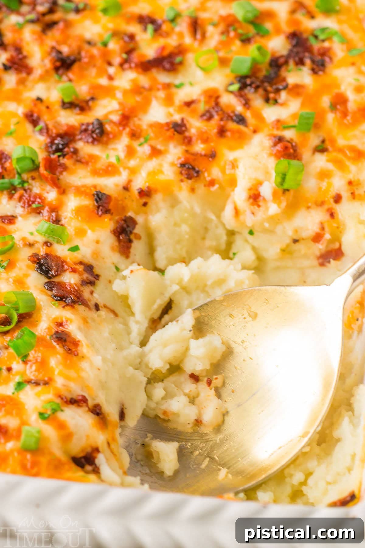 Velvety Potato Bake 6 Top down look at loaded mashed potato casserole recipe in a white baking dish with a gold serving spoon resting in the dish where a serving has been removed.