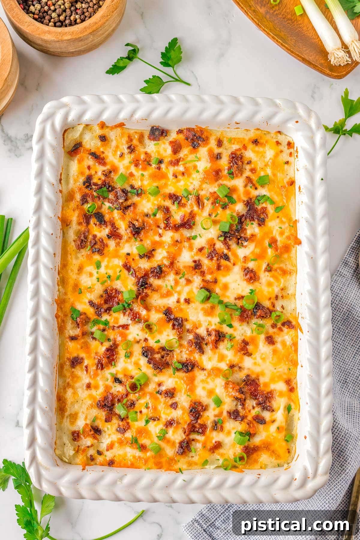 Velvety Potato Bake 7 Top down look at baked mashed potatoes in white casserole dish topped with cheese and bacon.
