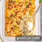 Top down look at mashed potato casserole in a white baking dish with a gold serving spoon resting in the dish where a serving has been removed.