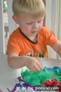 Close-up of hands tearing colorful tissue paper into small, irregular pieces.