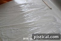 A popsicle stick spreading white glue evenly on one half of the wax paper.