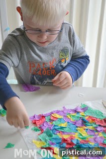 Hands carefully placing torn tissue paper onto the glue-covered wax paper, covering the entire area.