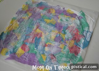 A finished tissue paper and wax paper sandwich being smoothed flat and placed under a heavy object to dry.