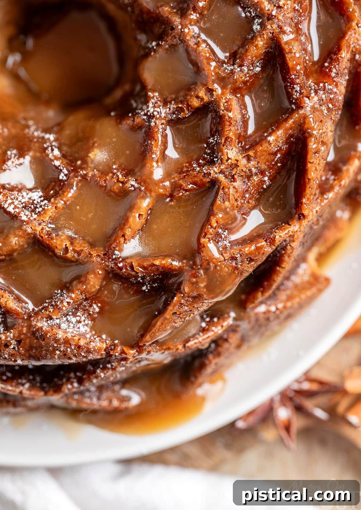 Top down view of a beautiful Caramel Apple Bundt Cake on a white cake plate, with shiny caramel glaze pooling around its intricate design.