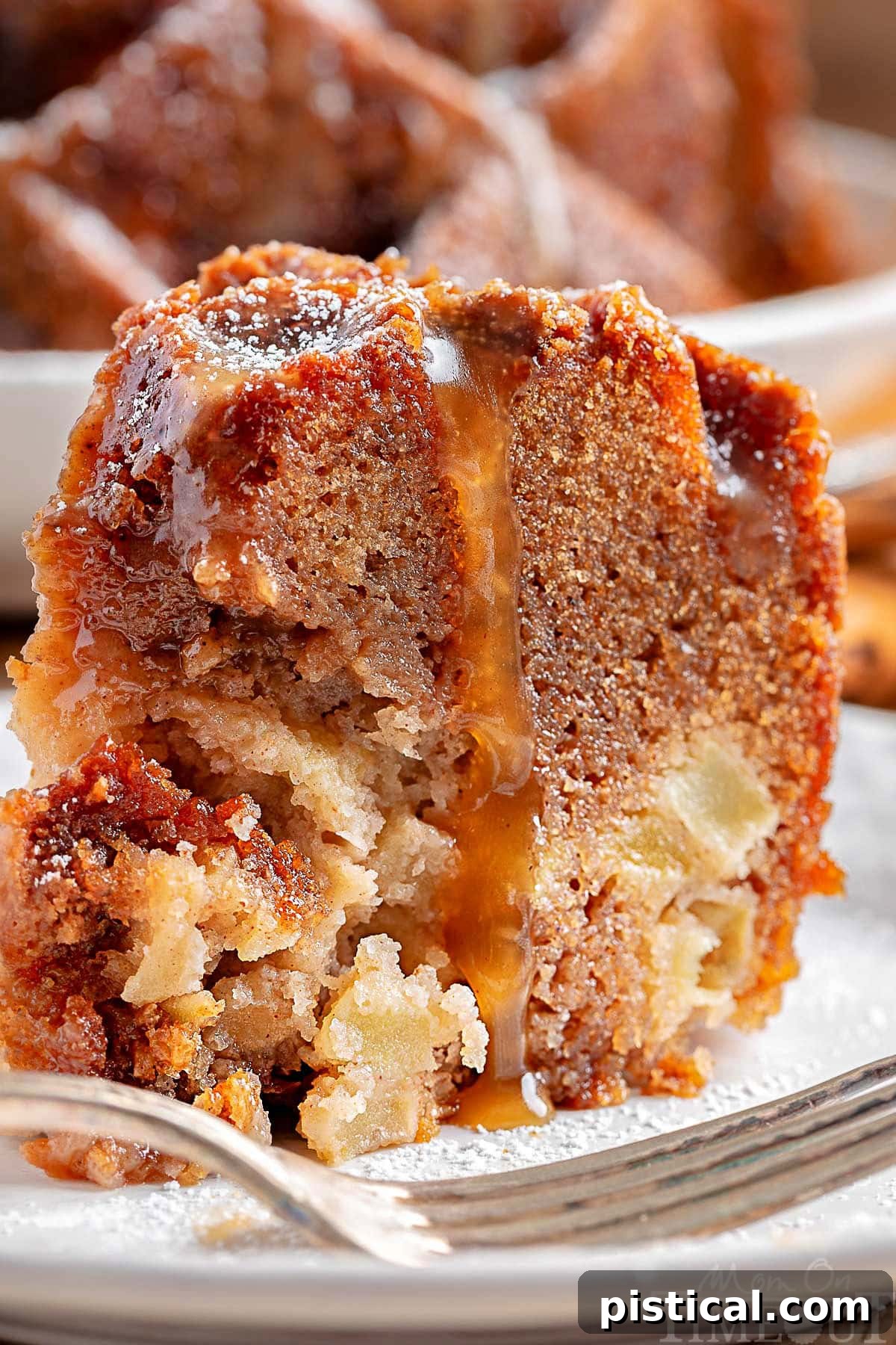 A close-up of a slice of Caramel Apple Bundt Cake, revealing its moist crumb and rich caramel glaze, with the rest of the cake blurred in the background.