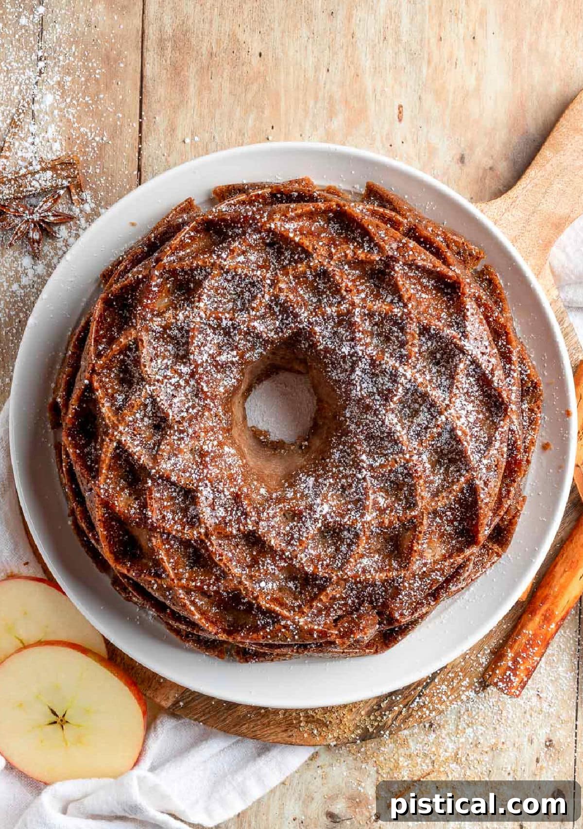 Top down view of the Caramel Apple Bundt Cake, lightly dusted with powdered sugar, sitting on an elegant white cake plate.
