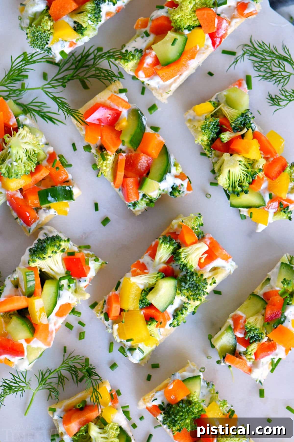 Close-up, top-down view of a freshly prepared veggie pizza, expertly cut into small, manageable pieces for serving. Scattered fresh dill sprigs adorn the elegant marble cutting board.