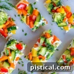top down view of veggie pizza recipe assemble and cut into small pieces for serving. dill sprigs are scattered about on the marble cutting board.