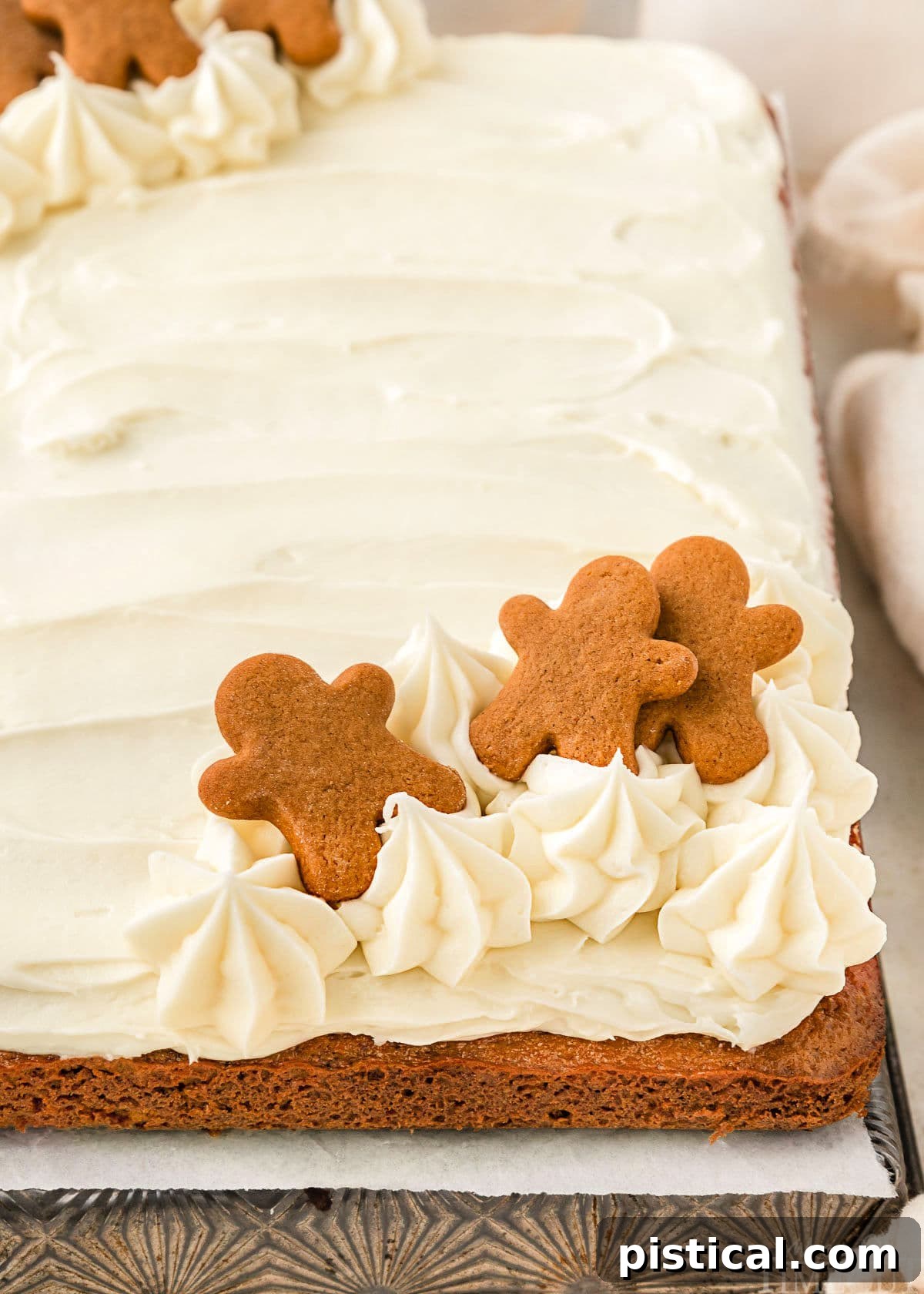 A beautiful side view of a moist gingerbread cake generously topped with fluffy cream cheese frosting and decorated with tiny gingerbread men.