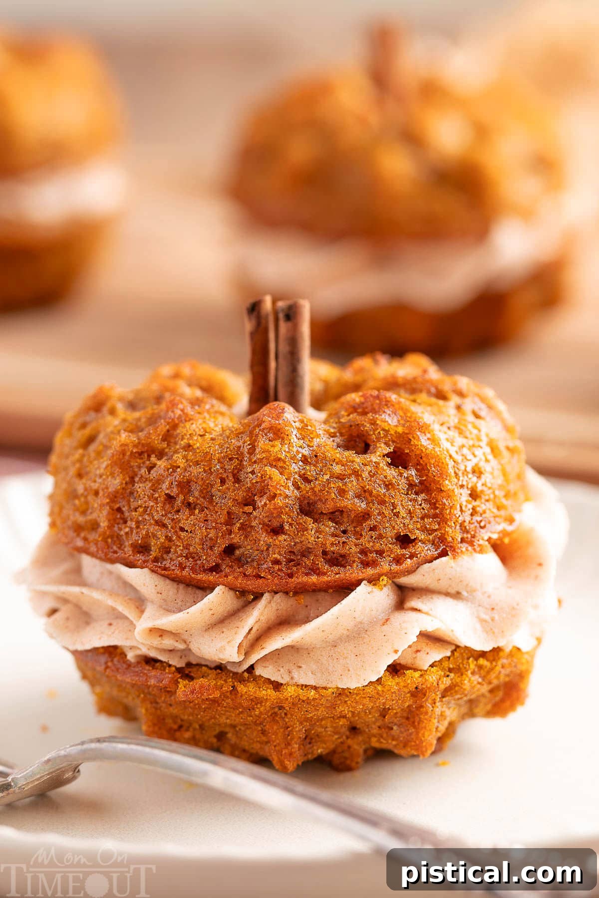Mini pumpkin bundt cake made with two small bundts and sandwiched with cinnamon brown butter frosting. The stem is a cinnamon stick. The cake is sitting on a white plate with a fork.