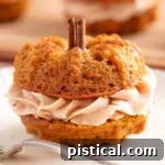 Mini pumpkin bundt cake made with two small bundts and sandwiched with cinnamon brown butter frosting. The stem is a cinnamon stick. The cake is sitting on a white plate with a fork.