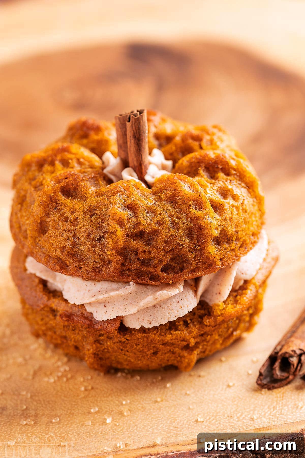 Mini pumpkin bundt cake made with two small bundts and sandwiched with cinnamon brown butter frosting. The stem is a cinnamon stick. The cake is sitting on a wood board.