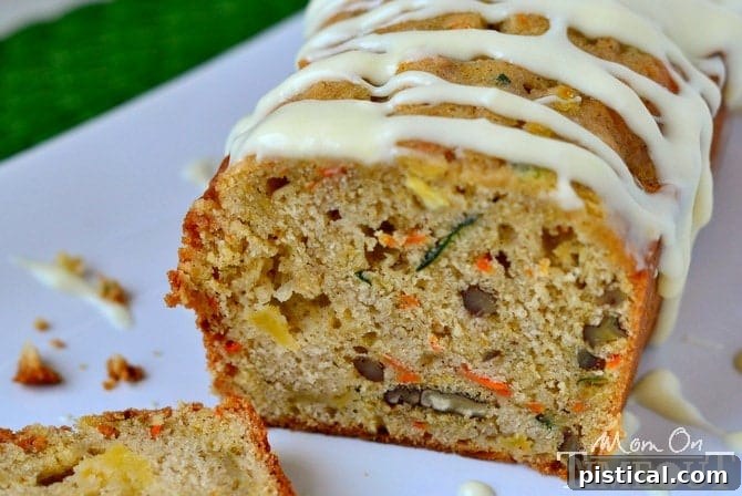 A slice of moist Carrot Zucchini Apple Bread topped with creamy, tangy cream cheese frosting, ready to be enjoyed.