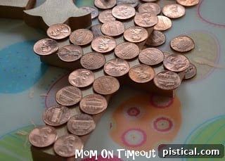 Arranging pennies on a copper-painted cross, carefully planning the coin layout before gluing