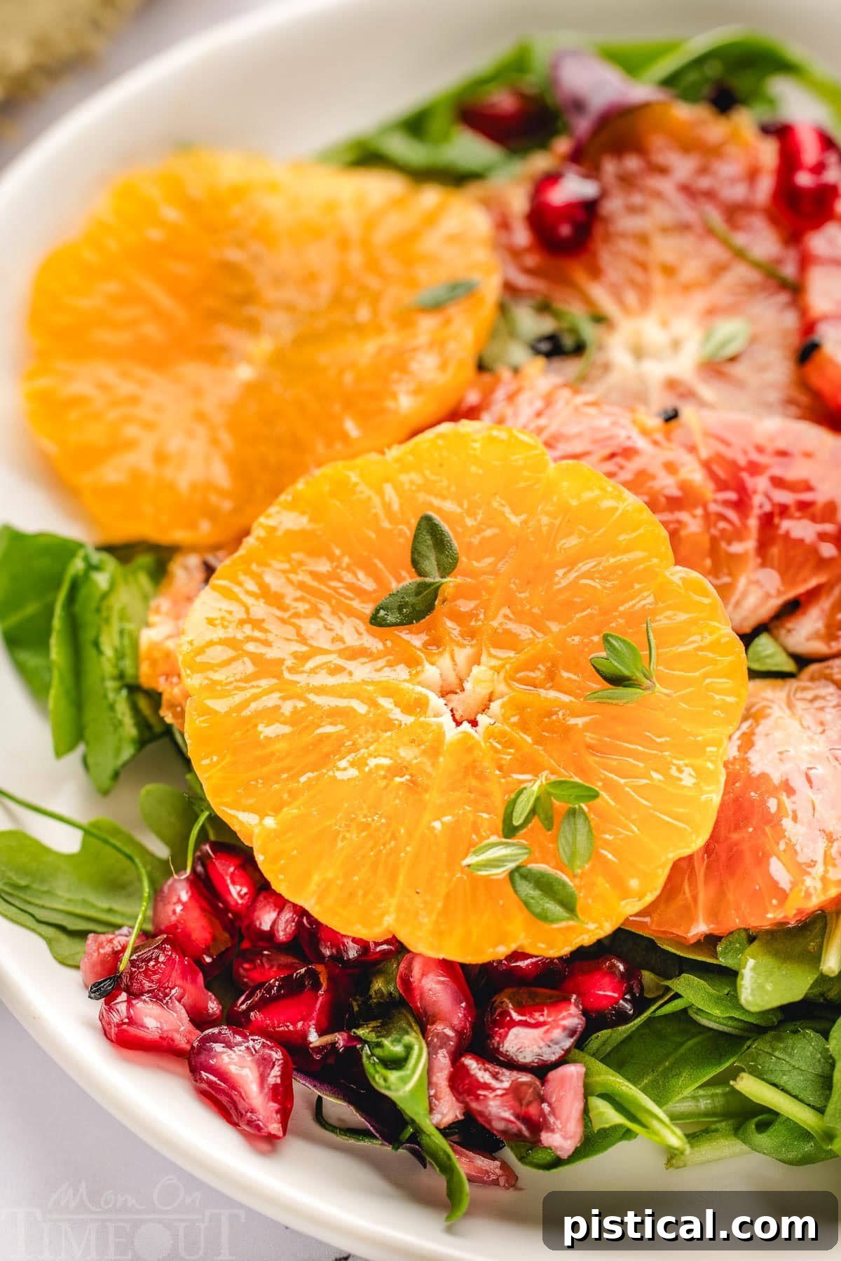 Close up of orange slices, arugula, pomegranate seeds all tossed with dressing for citrus salad.