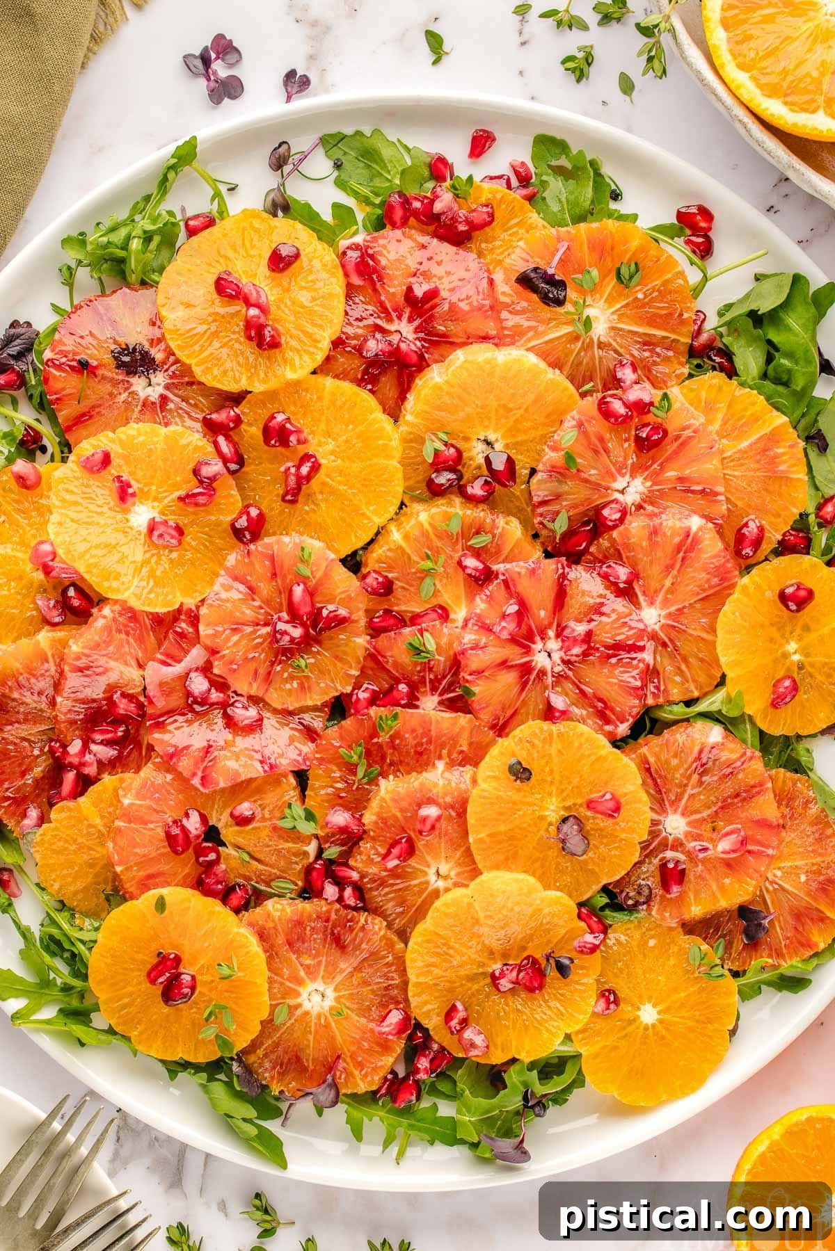 Close up look at citrus salad on white round platter ready to be served. Pomegranate seeds top the citrus rounds and arugula base.
