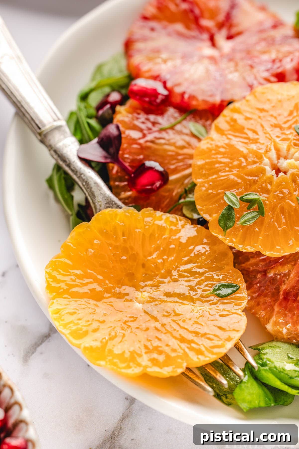 Close up of orange slices, arugula, pomegranate seeds all tossed with citrus salad dressing.
