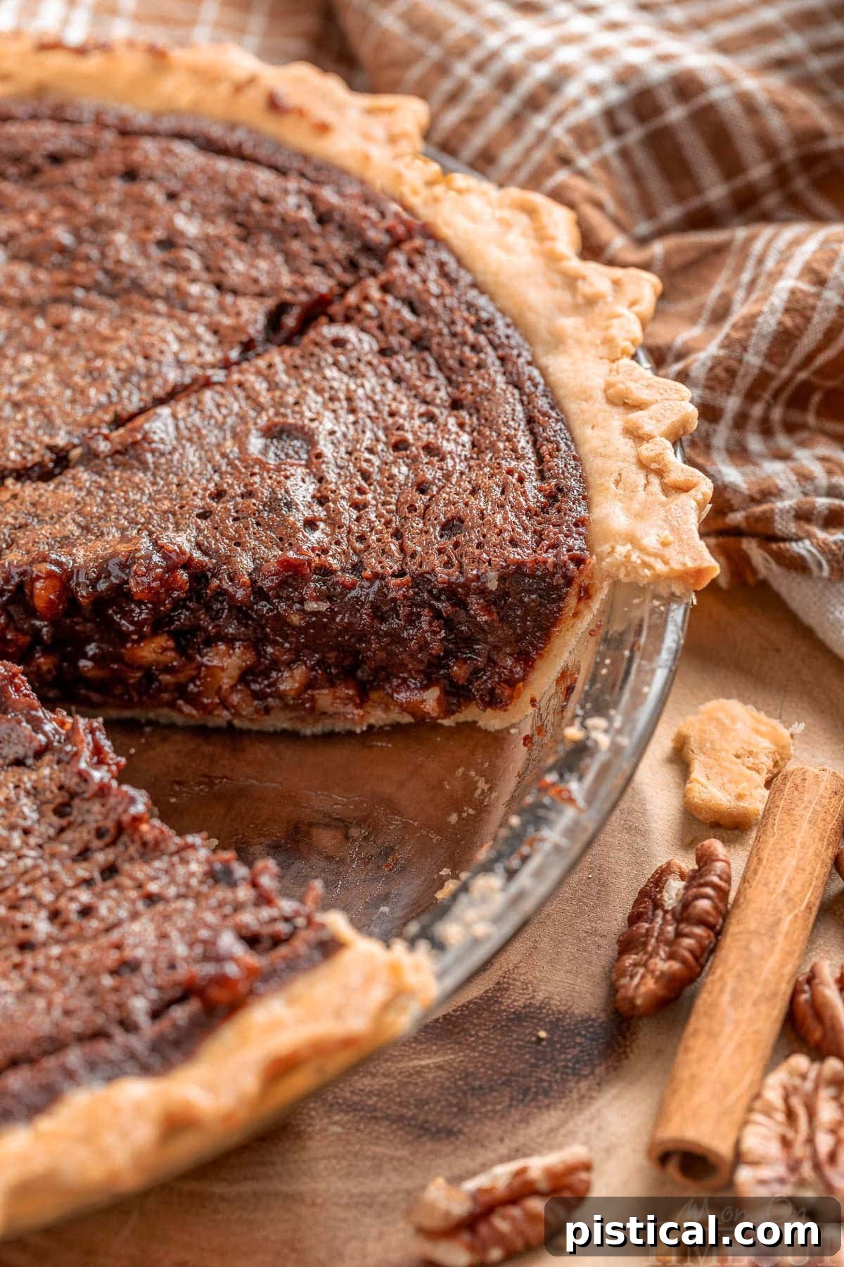An inviting angled view looking down on a whole Chocolate Bourbon Pecan Pie, with one perfect slice carefully removed, revealing the rich, layered interior of chocolate, pecans, and gooey filling.
