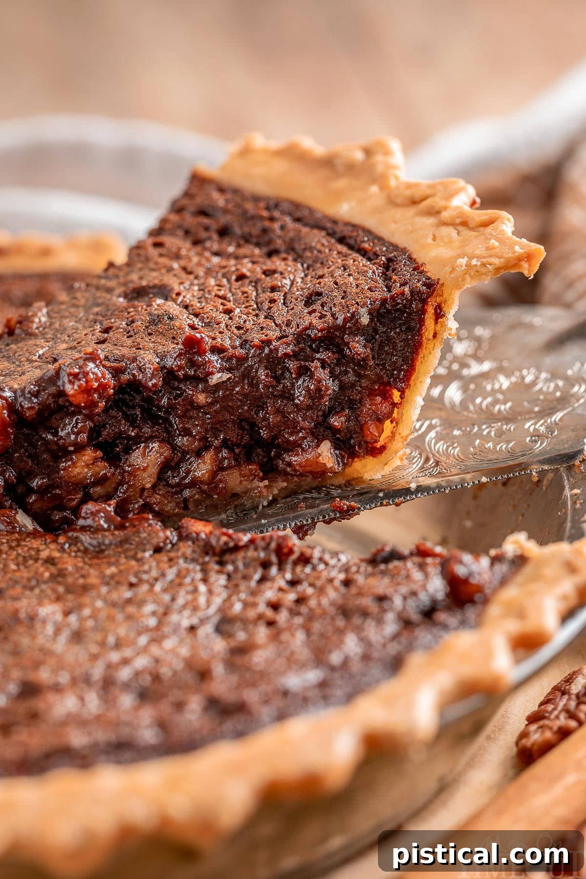 A perfect slice of Chocolate Pecan Pie with Bourbon being gently lifted out of the pie plate, showcasing its golden crust and rich, dark filling.