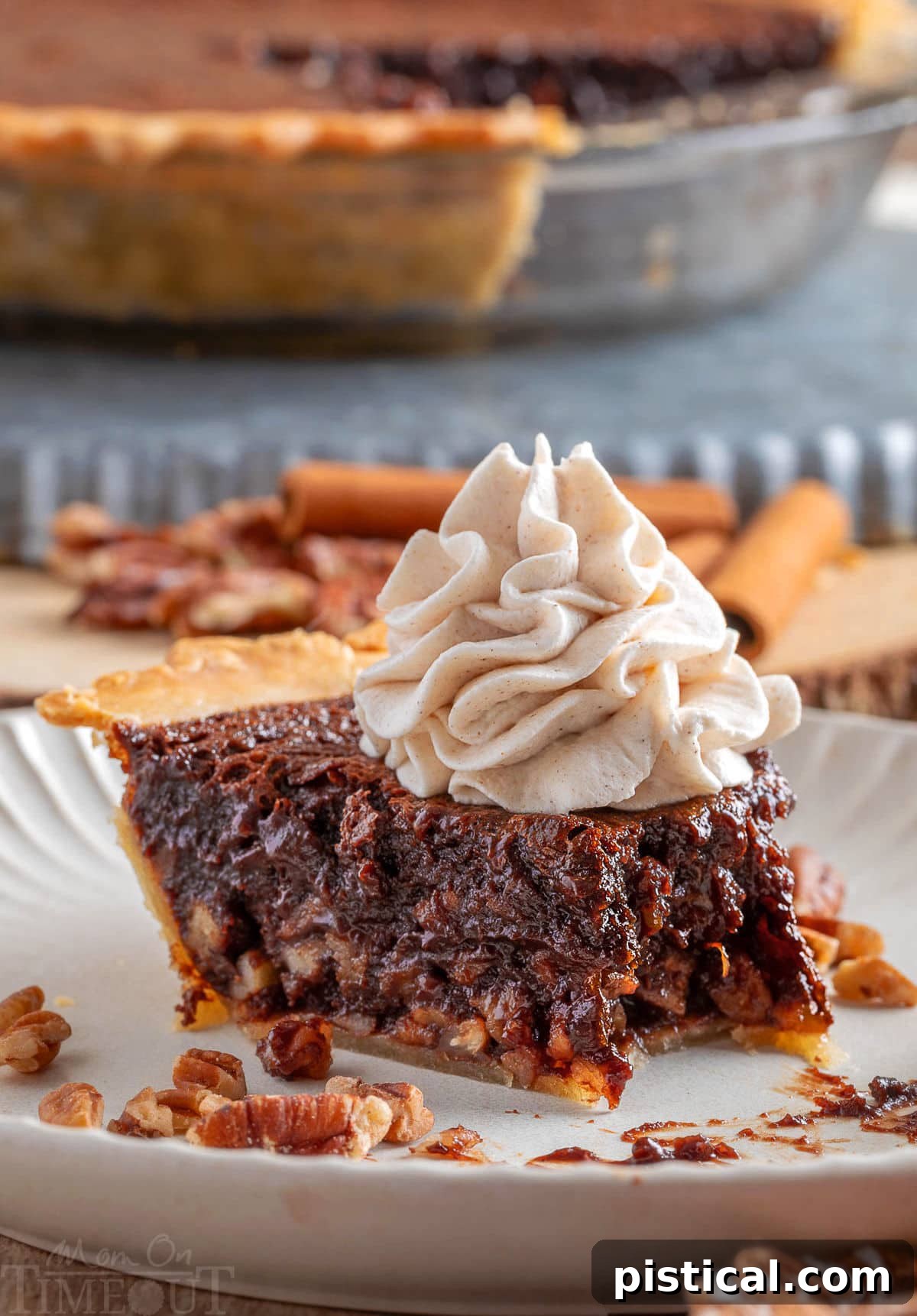 A generous slice of Chocolate Bourbon Pecan Pie on a white plate, topped with creamy whipped cream. A bite has been taken from the end, revealing the delicious layers. The remaining pie is visible in the background.