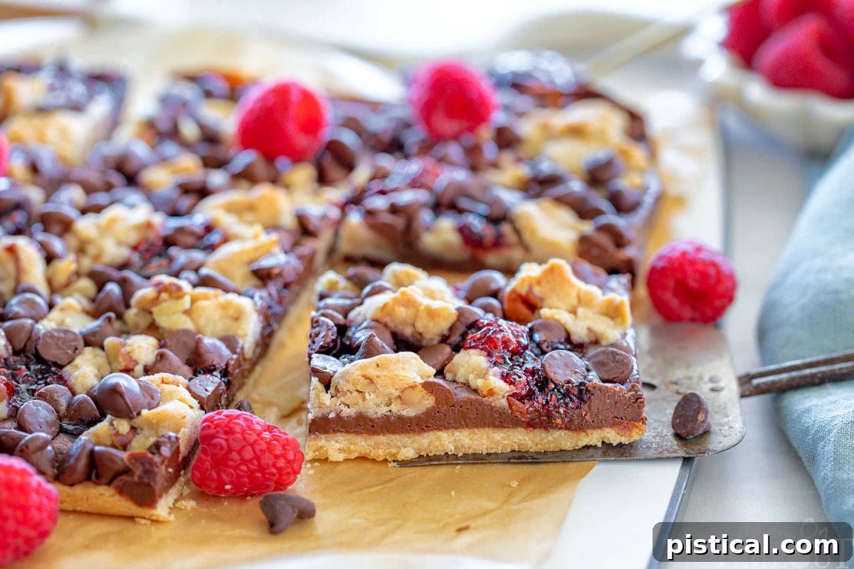 A single chocolate raspberry crumb bar being carefully lifted away from a slab of freshly baked bars on a cutting board, showcasing its perfect layers.