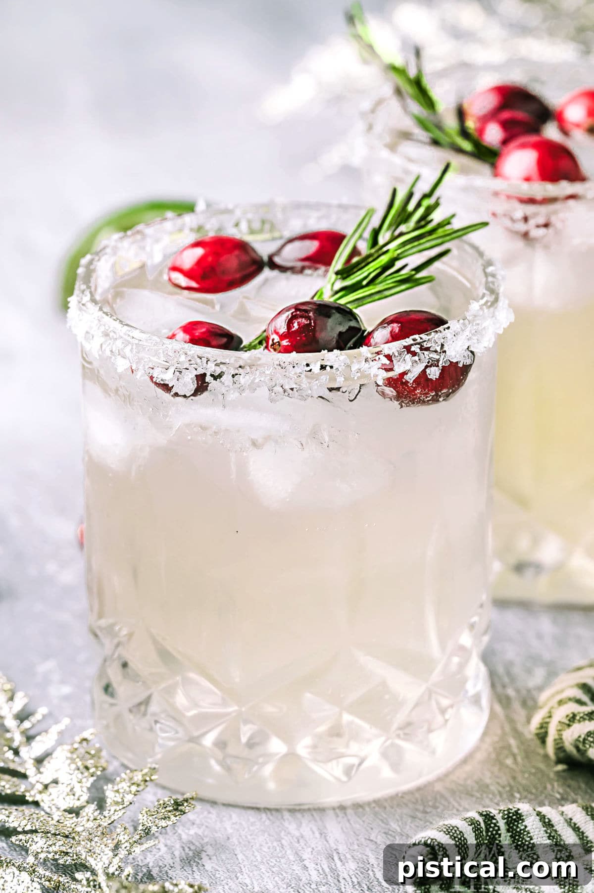 Christmas margarita in a short glass topped with fresh cranberries and a sprig of rosemary, Another glass can be seen in the background.