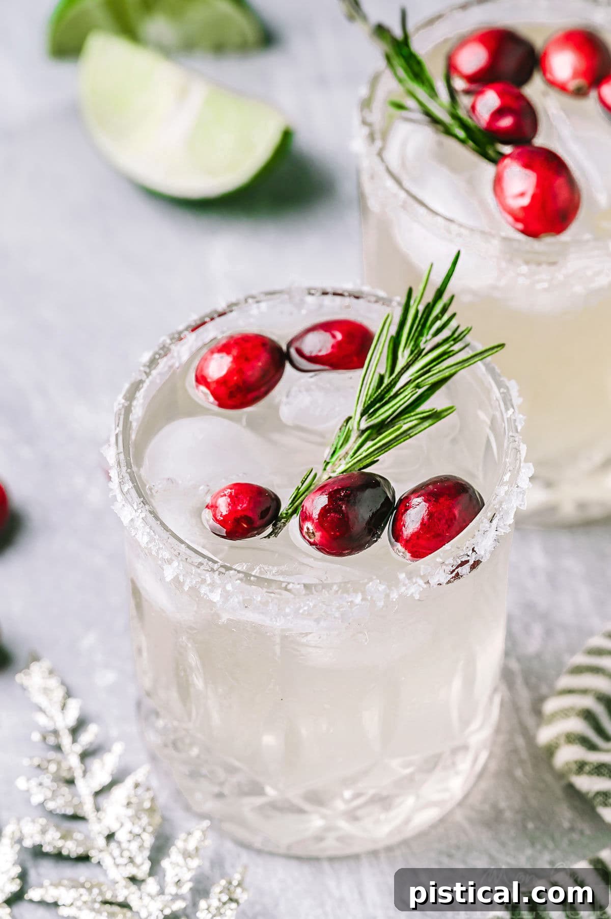 Angled down look at Christmas margaritas in short glasses with a sugared rim. The margaritas are garnished with fresh cranberries and rosemary.
