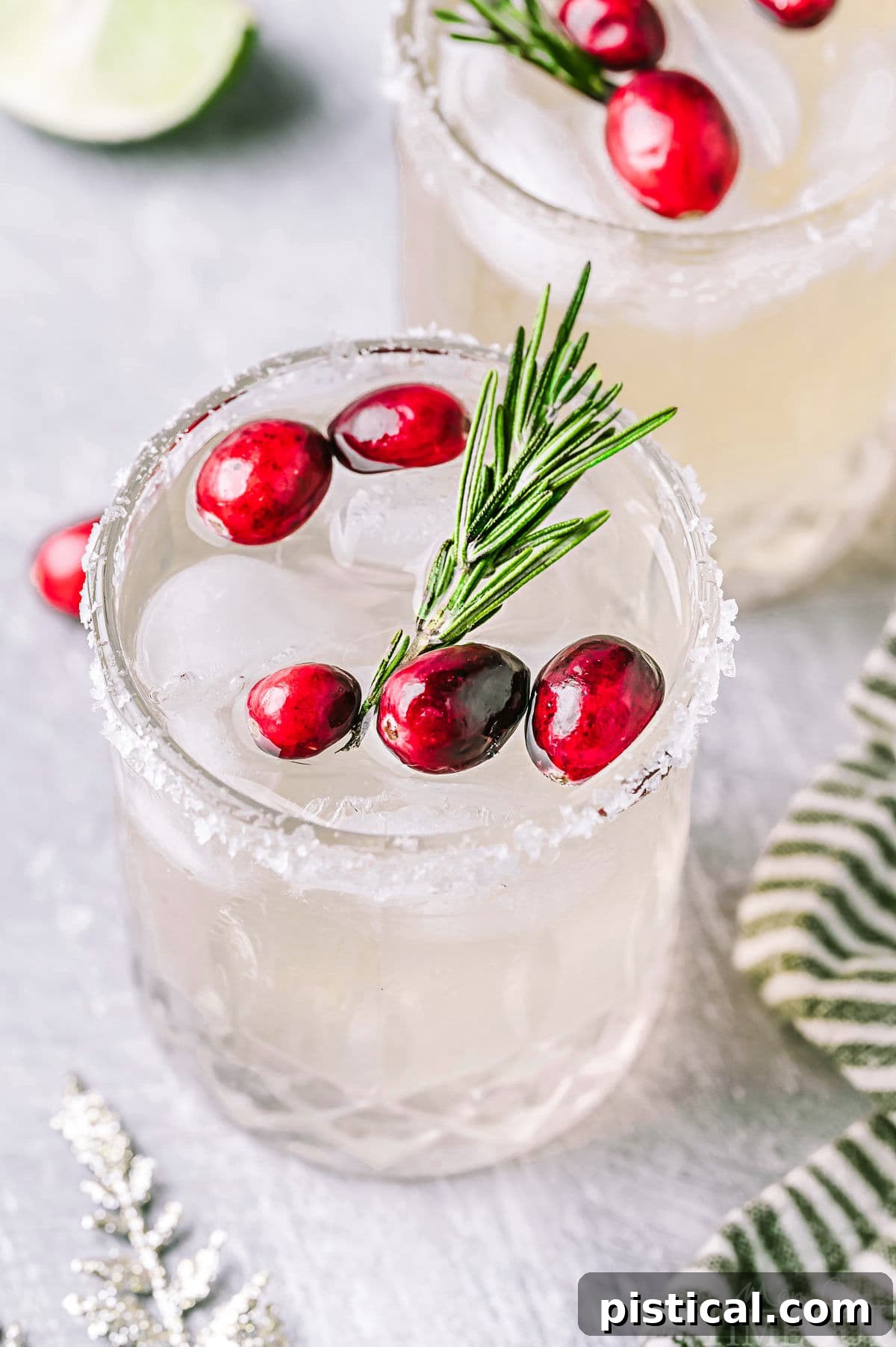 Angled down look at Christmas margaritas in short glasses with a sugared rim. The margaritas are garnished with fresh cranberries and rosemary.