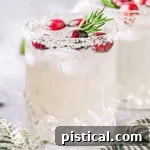 Christmas margarita in a short glass topped with fresh cranberries and a sprig of rosemary, Another glass can be seen in the background.
