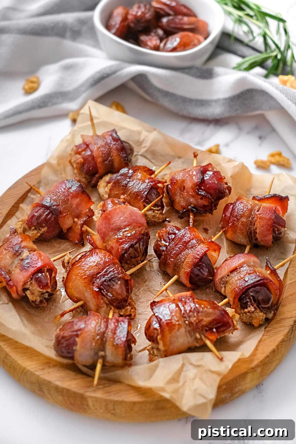 Wood serving tray topped with brown parchment paper and bacon wrapped dates ready to be enjoyed. The dates still have the toothpicks in them making them easy to pick up.