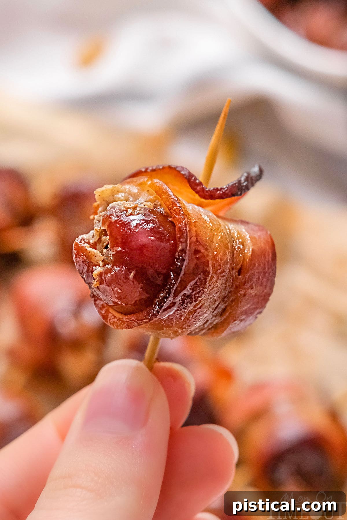 Bacon wrapped date being held up with a toothpick through the date.