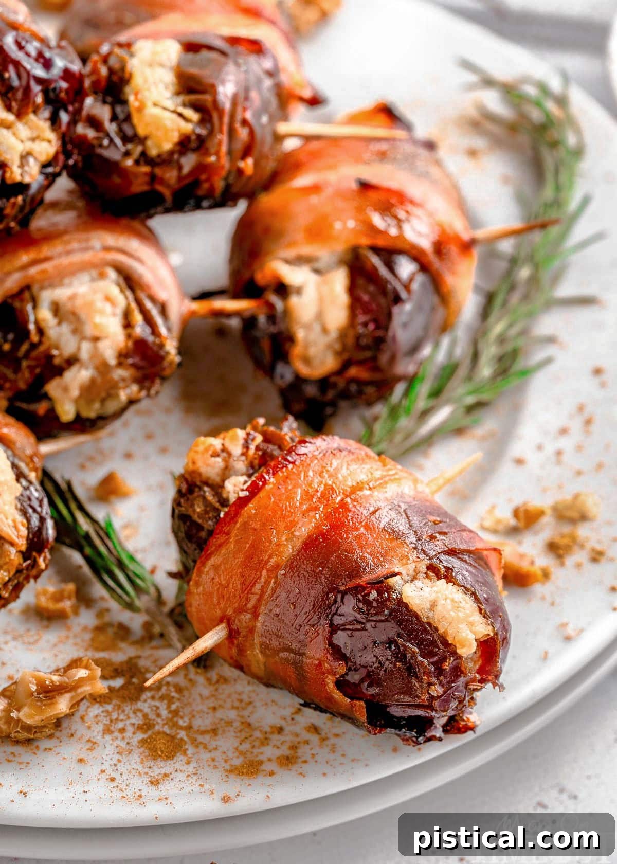 Shot of dates wrapped in bacon served on round white plate garnished with rosemary.