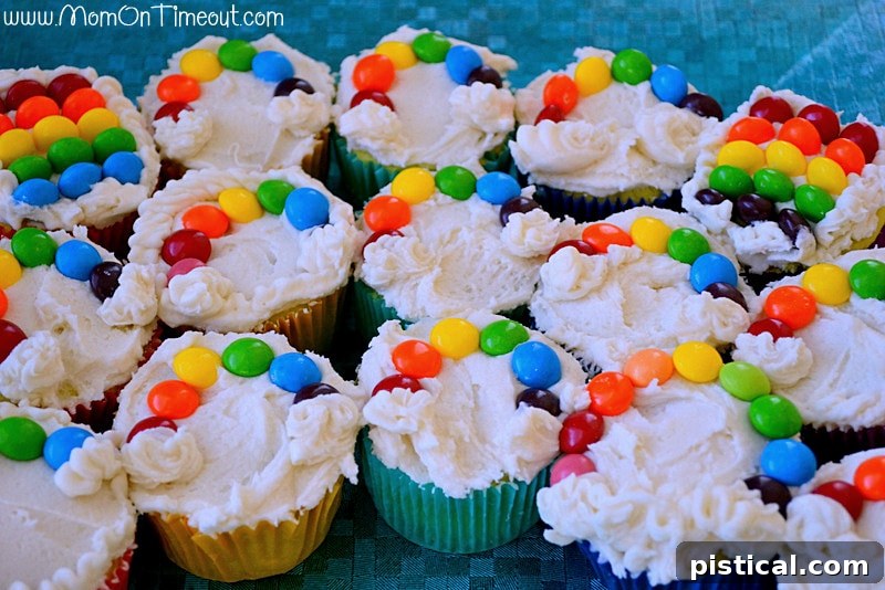 Close-up shot of several Taste the Rainbow Cupcakes, showcasing colorful Skittles arranged like rainbows on white frosting