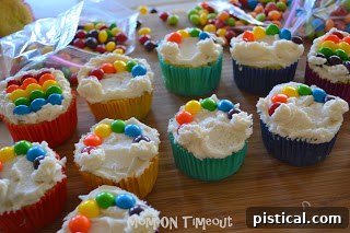 A child's hands carefully placing Skittles to form a rainbow arc on a frosted cupcake