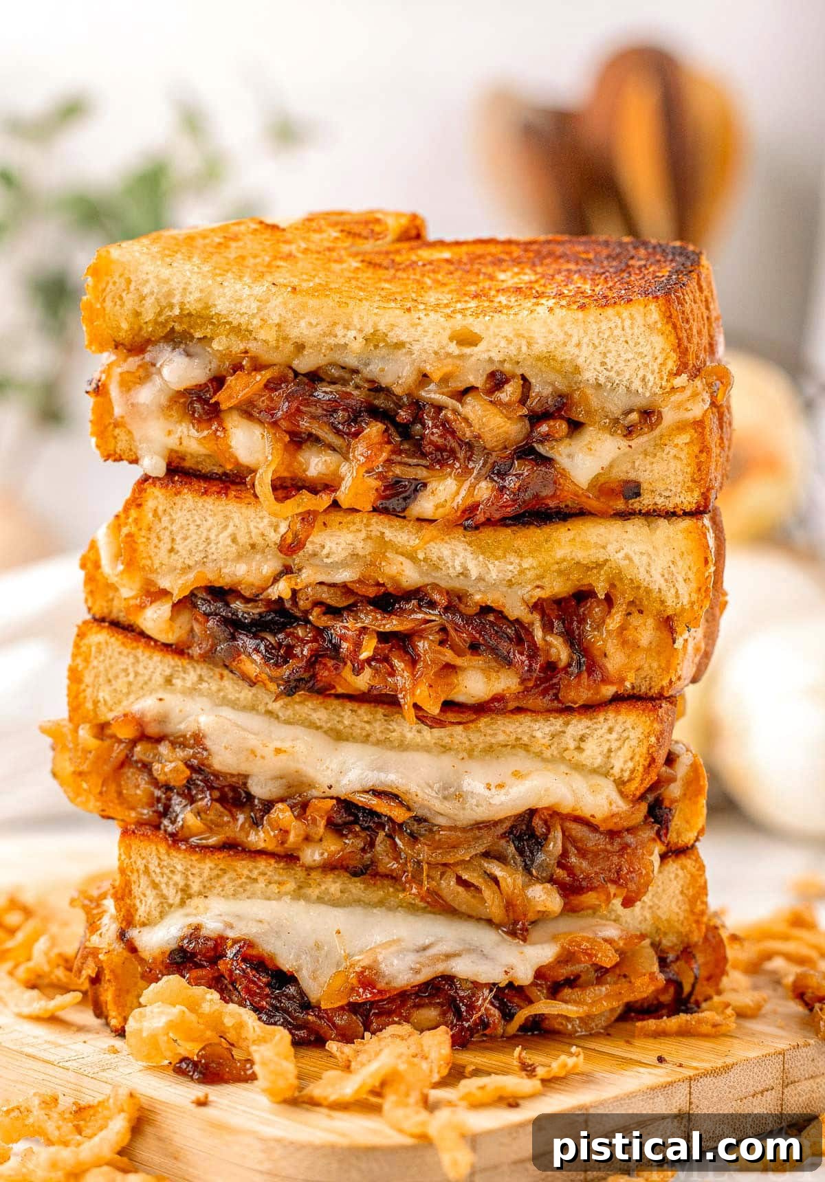Tall stack of french onion soup grilled cheese cut in half on wood cutting board. Golden brown bread and gooey cheese can be seen along with the caramelized onion filling in the sandwiches.