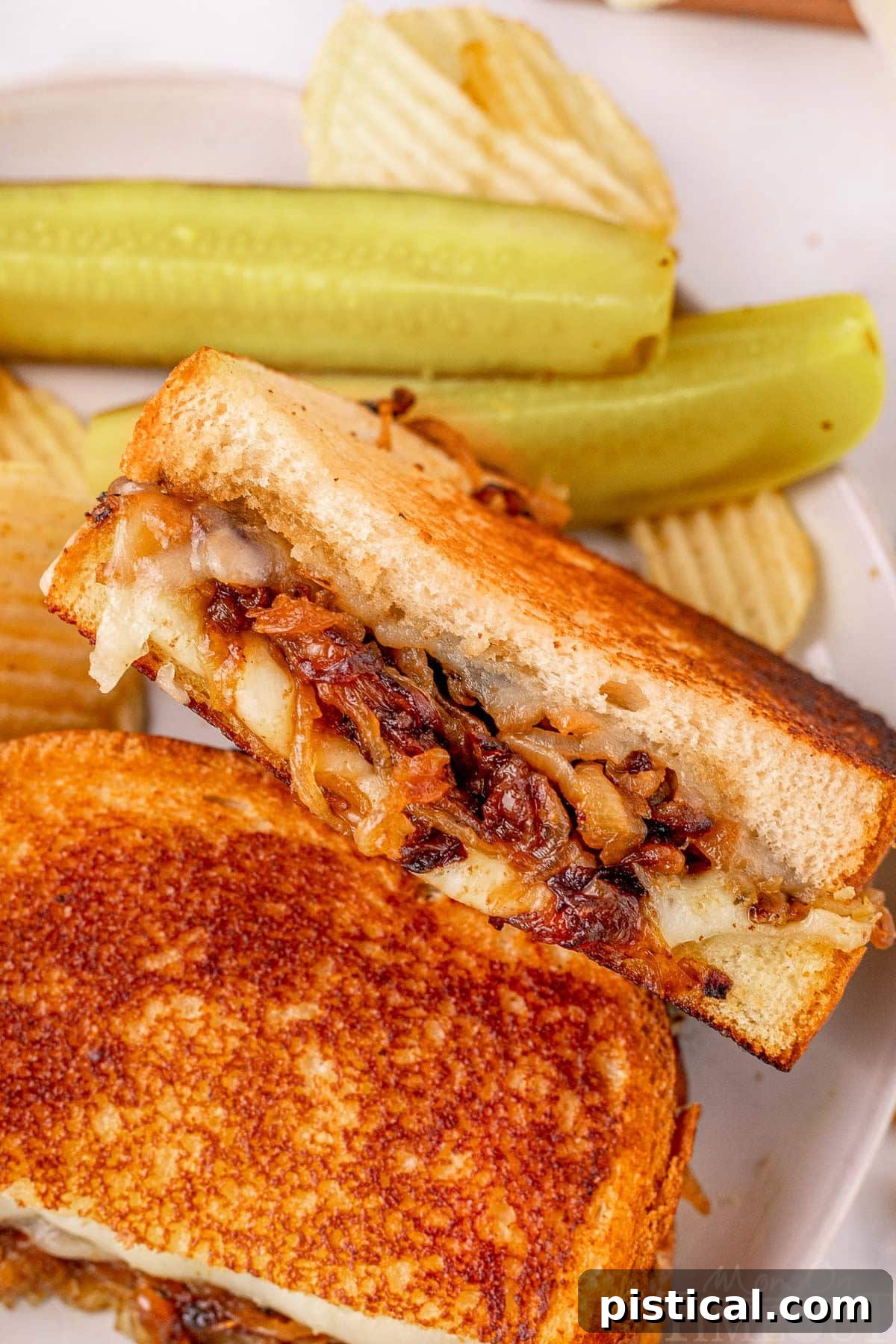French Onion soup grilled cheese sandwich cut in half on a plate with pickle spears and chips.