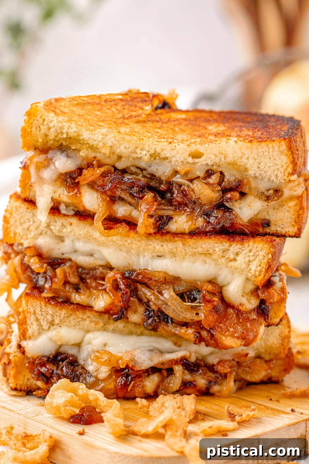Three halves of a french onion grilled cheese sandwich stacked on a wood cutting board with french fried onions surrounding it.