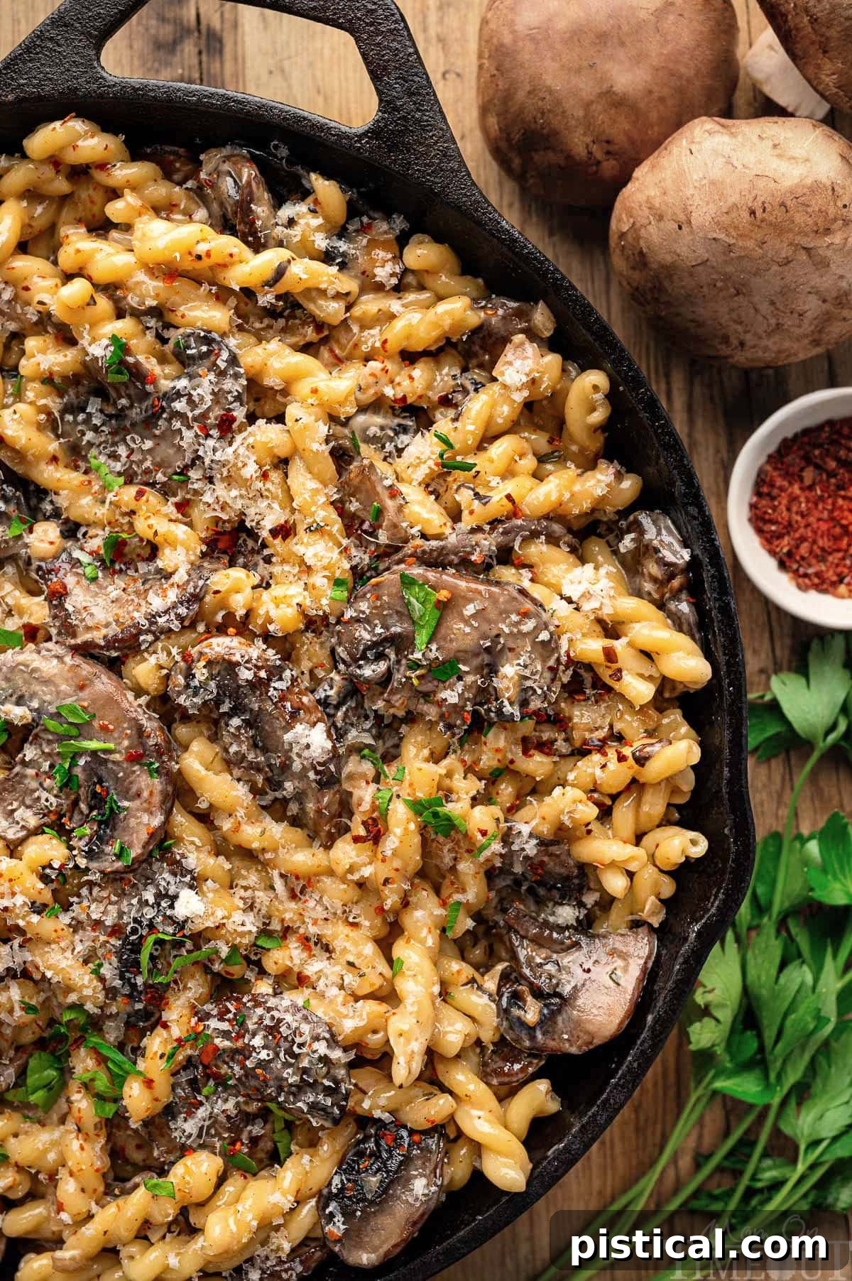 Close up look at mushroom pasta sauce recipe in a cast iron skillet sitting next to mushrooms and herbs.