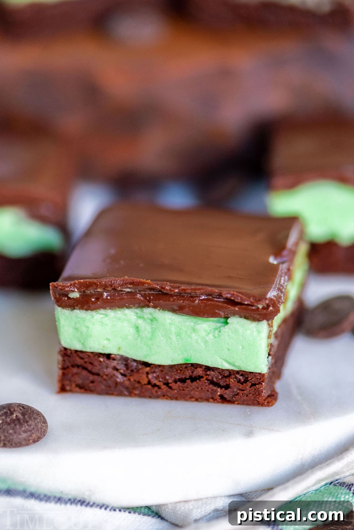 A single chocolate mint brownie sitting on a marble surface, perfectly showcasing its three distinct layers, with more brownies visible in the background.
