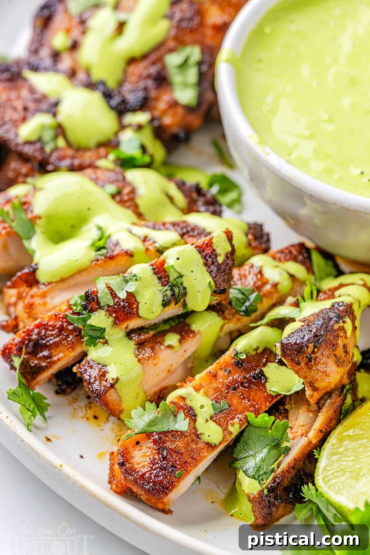 Close up view of slices of Peruvian Chicken drizzled with Aji Verde on a white serving plate.
