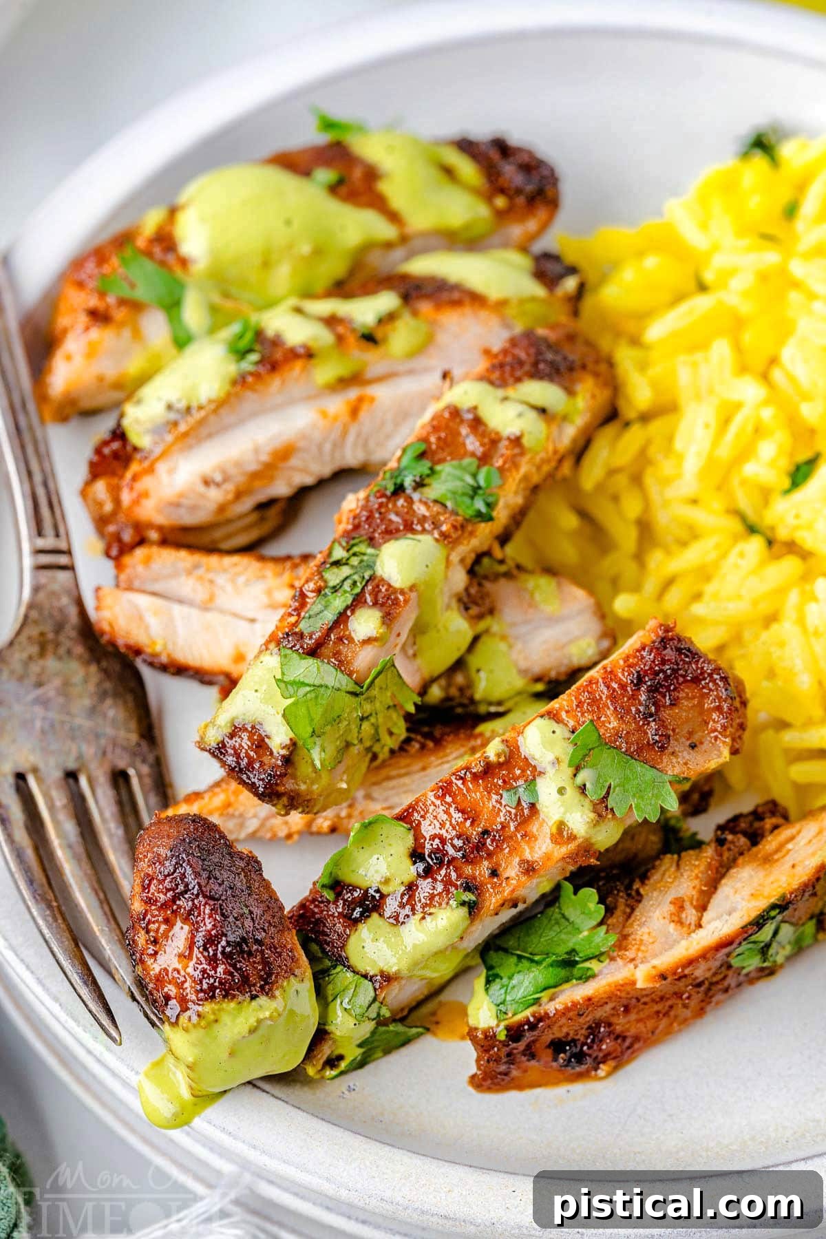 Sliced Peruvian Chicken next to a side of rice on a white plate with a fork holding a piece.