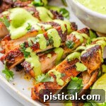 Close up view of slices of Peruvian Chicken drizzled with Aji Verde on a white serving plate.