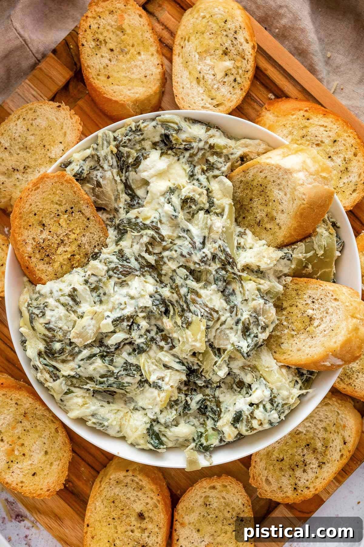 Crockpot spinach artichoke dip in a white bowl surrounded by crostini.