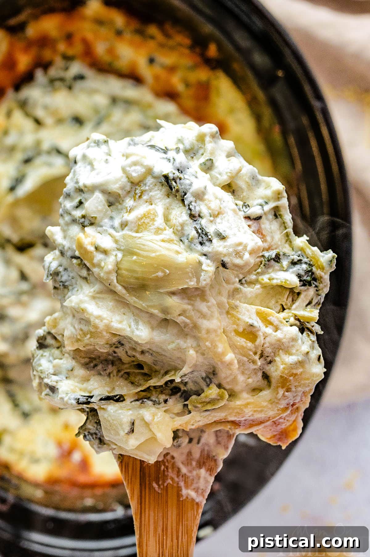Crockpot spinach and artichoke dip scooped up with a large wooden spoon.