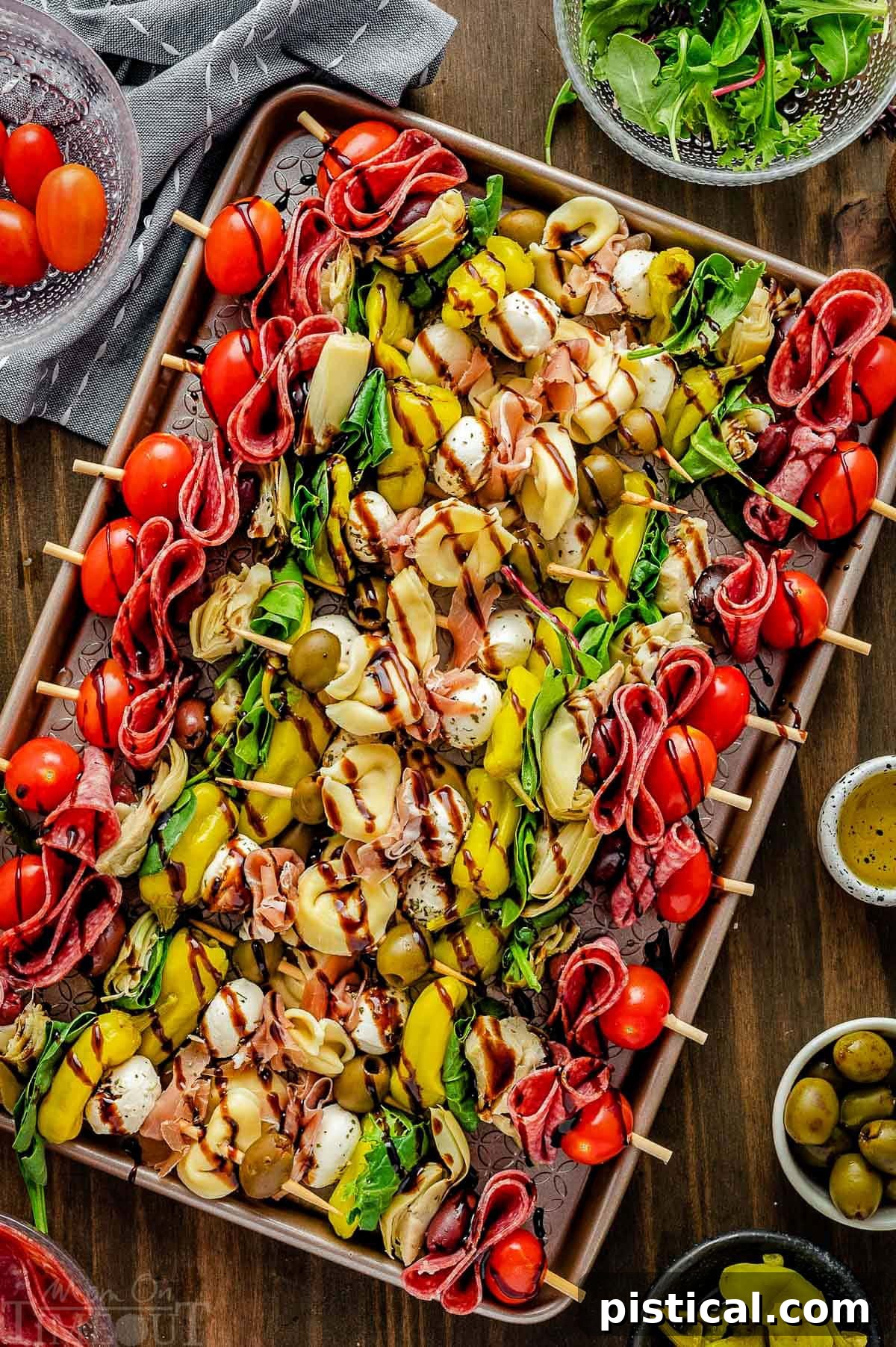 Top down view of colorful antipasto skewers arranged on a sheet pan, lightly drizzled with balsamic glaze and ready for serving at a party.