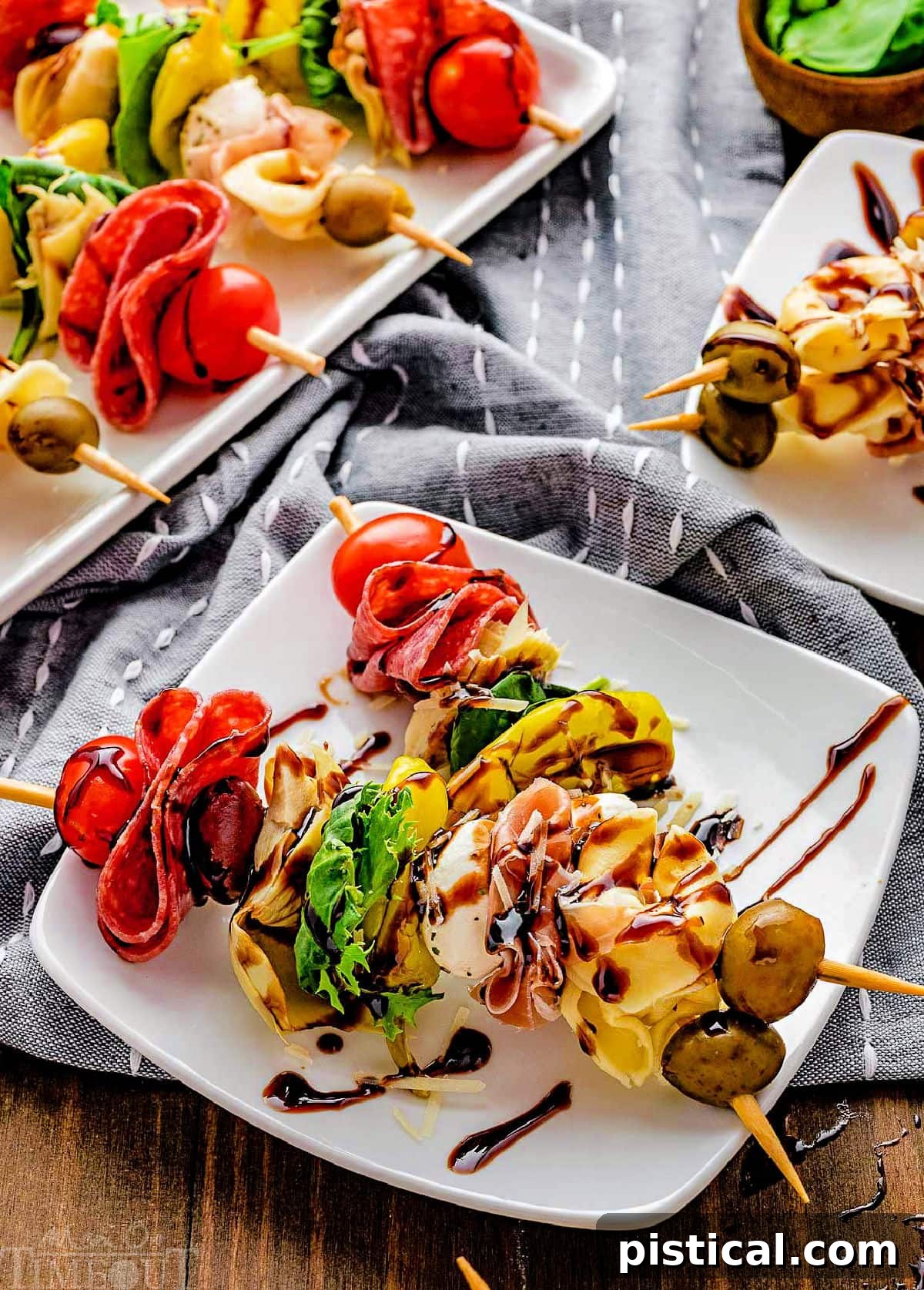 Two perfectly assembled antipasto skewers artfully arranged on a clean white plate, glistening with a balsamic glaze drizzle.